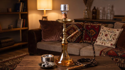 Narguilé traditionnel en verre et laiton posé sur une table basse avec un cendrier en inox et une coupelle de charbons refroidis