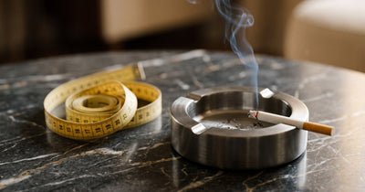 Cendrier en metal design avec une cigarette allumee et un metre ruban sur une surface en marbre sombre illustrant le lien entre tabac et poids