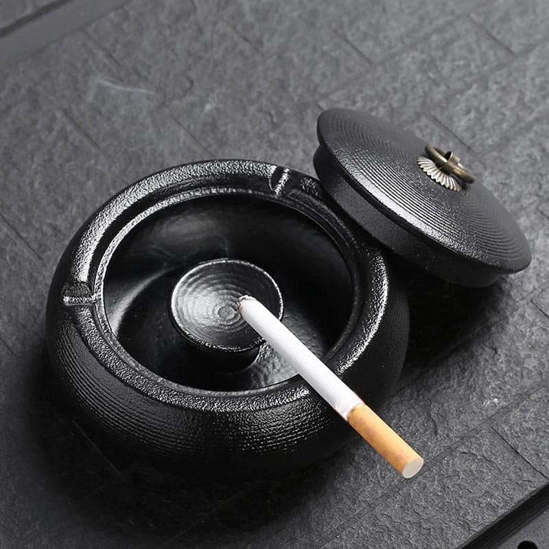 Cendrier noir inox avec cigarette posée sur le rebord
